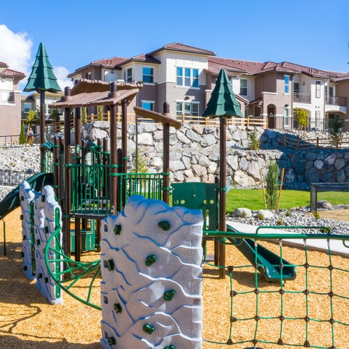Apartments For Rent In Reno Nevada - Vida - Playground With Wood Chips, Swings, Slides, Climbing Equipment, And View Of Apartment Buildings In The Background.